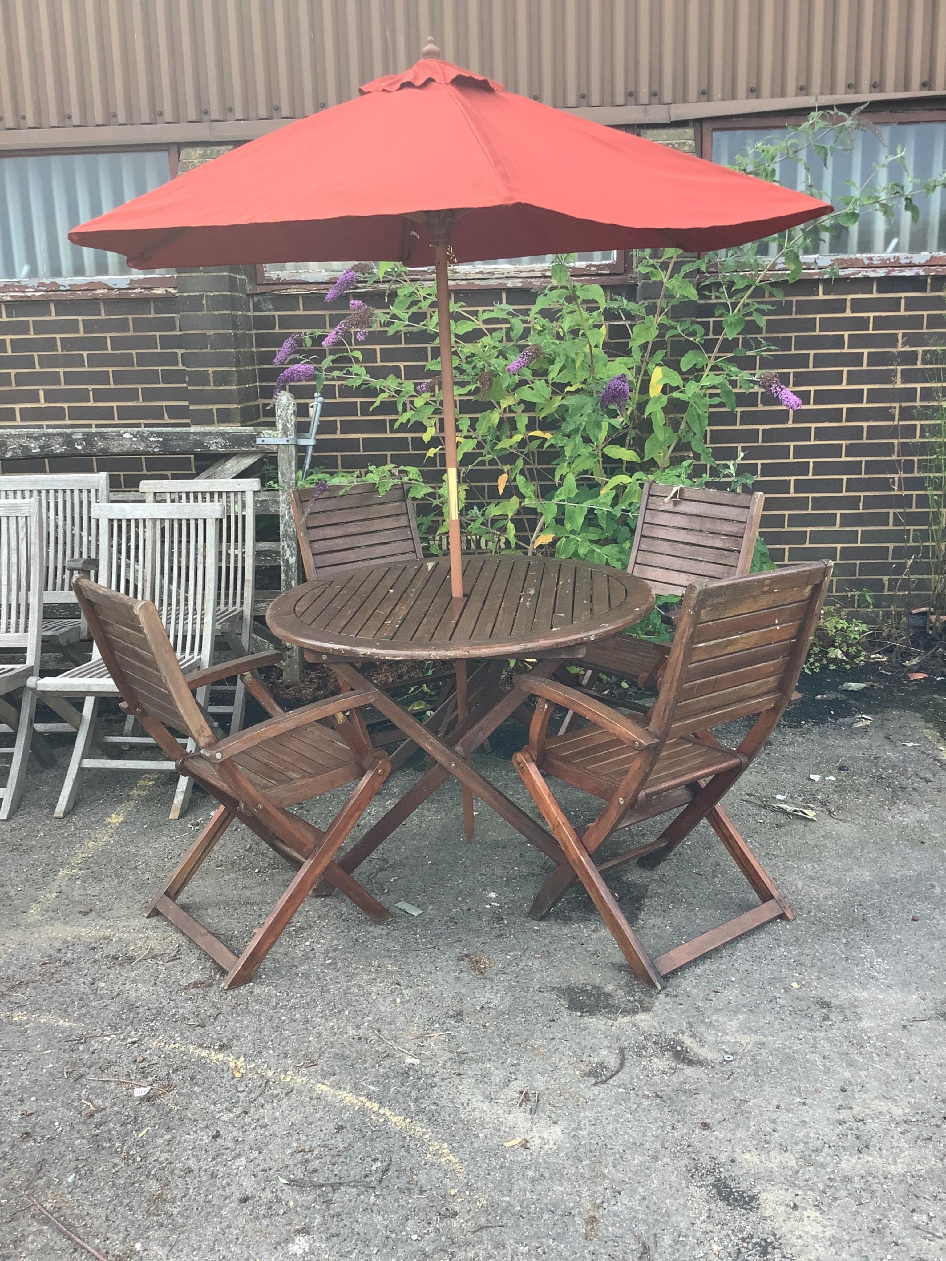 A stained teak circular folding garden table, diameter 106cm, height 75cm together with four folding garden elbow chairs and a canvas parasol. Condition - poor-fair